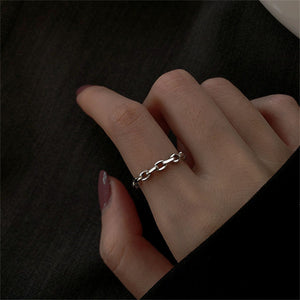 Silver chain ring on a finger against a dark background