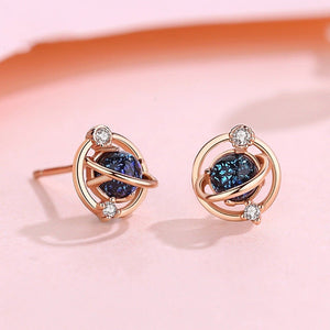 Pair of rose gold earrings with blue gemstones on a pink background