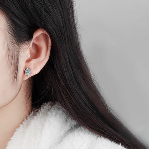 Woman wearing sea turtle-shaped earrings with gemstones on a white background