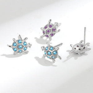 Set of sea turtle-shaped earrings with gemstones on a white background