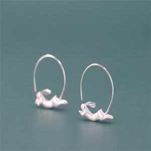 A pair of gold-colored hoop earrings with a small bunny rabbit design on a red background.