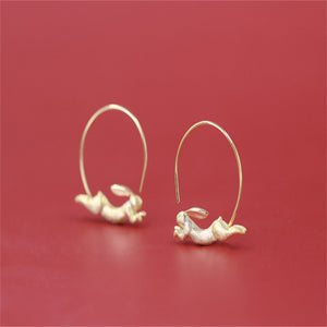 Gold hoop earrings with small decorative elements on a red background