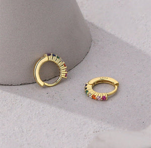 Gold hoop earrings with colorful gemstones on a gray surface
