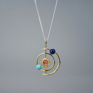 Gold pendant with sun, moon, and star design on a gray background