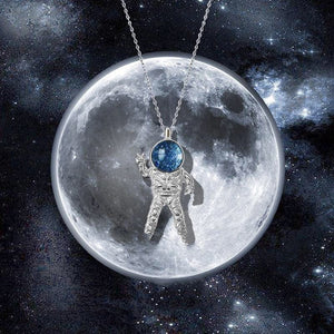 A sterling silver necklace with a blue glass pendant featuring a spaceman and a planet, set against a starry background.