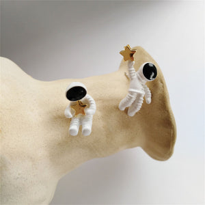Pair of astronaut earrings on a beige stand with a plain background