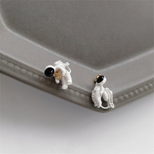 A pair of silver-colored stud earrings featuring a spaceman and star design, displayed on a mannequin bust.