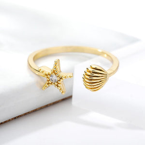 Gold ring with starfish and shell designs on a white background.