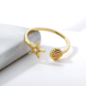 Gold ring with starfish and shell designs on a white background.