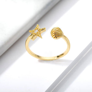 Gold ring with starfish and shell designs on a white background.