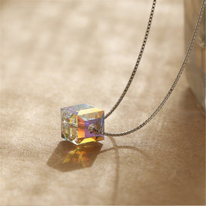 Crystal cube pendant on a chain against a beige background