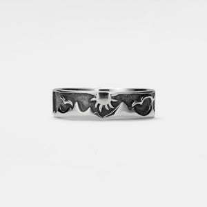 Silver ring with decorative sun and mountain design on a light gray background