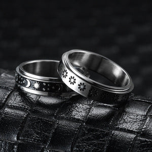 Two silver rings with intricate designs on a textured black surface