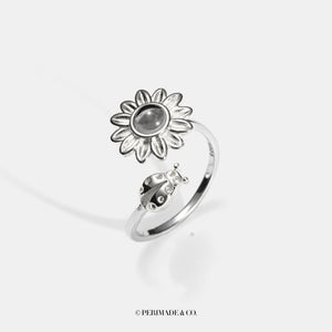 Silver sunflower-shaped ring with a central projection gemstone on a white background