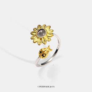 Gold sunflower-shaped ring with a central projection gemstone on a white background