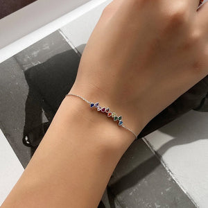Model wearing a sterling silver bracelet with multicolored gemstone accents, displayed on an open book.