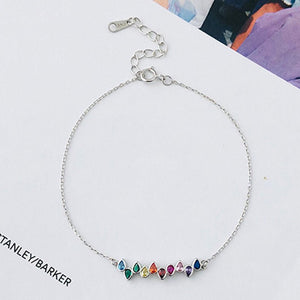 Sterling silver bracelet with white gold plating and multicolored gemstone accents, displayed on an open book.