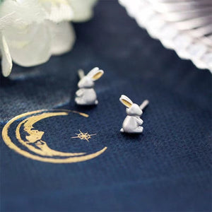 Silver rabbit earrings on a blue fabric background with gold crescent moon and star design.